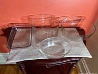 Full view of four clear glass kitchen items on a small table against orange wall.