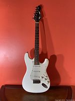 Full view of the Dean electric guitar against red background showing the white and cream body and dark wood neck.