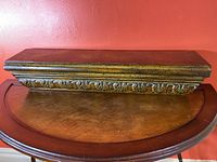 Front view of painted tin floating shelf showing ornamental trim detail and aged gold finish