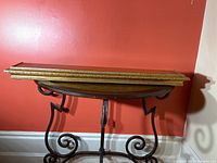 Gold ornate lightweight floating shelf resting on a decorative metal table against red wall.