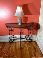 Full view of half moon table with wood top and black metal scroll base, against a red wall background.