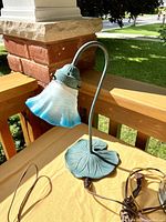 Green metal Lilly pad table lamp with curved stem and frosted glass shade with blue tint.