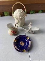 Photo of the lot showing a blue and gold Limoges ashtray, white Partylite basket with handle, floral creamer, and floral dish.