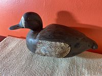 Side view of the painted wood duck decoy showing full profile on textured surface with orange wall background.