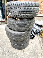 Stack of 4 used 55R15 tires showing tread and general condition outdoors against brick wall.