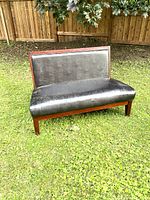 Photo of a wood framed bench upholstered in black leather, placed outdoors on grass, showing back and seat.