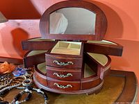 View of the wooden layered jewelry box with drawers, open side fold-out velvet-lined trays, top ring holder compartment, and hinged mirror showing reflections.