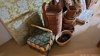 Wide view showing assorted various woven baskets arranged near a wall, including a tall cylindrical basket, picnic basket, and smaller baskets.