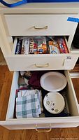 Open kitchen drawer showing storage baggies, plastic wrap, aluminum foil boxes, and disposable paper plates, dish towels inside drawers
