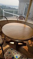 Round wooden dining table near window with surrounding chairs and visible scratches on tabletop surface.