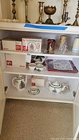Shelf showing boxed Spode Christmas tree dinnerware, cups, teapot, and several brass candlesticks above