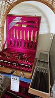Opened wooden case with pink velvet lining showing bronze knives with dark handles arranged in holders.