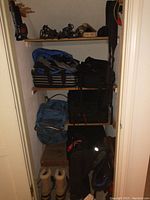 Closet with shelves holding luggage bags and ski gear including boots, poles, bindings, gloves, and bags