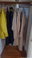 Coats and rain jackets hanging on a rack in closet, various colors including yellow, black, beige, and checked pattern