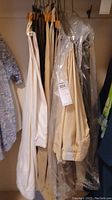 Hanging men's pants in beige, tan, and off-white colors with some protected in plastic garment bags