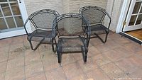 Set of four black metal mesh patio chairs arranged on a tiled outdoor floor.