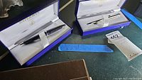 Two Waterman pens each in their original blue and white presentation boxes on a green surface.