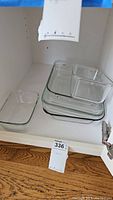 Clear Pyrex glass baking dishes stacked inside a white cabinet, showing four dishes including one square dish and three rectangular dishes of varying sizes.