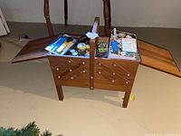 Overall view of open wooden fold-up sewing box showing compartments filled with sewing supplies and notions.