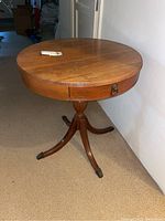 Photo of the vintage wood drum table showing round wooden top, single drawer with metal handle, and tripod pedestal base with claw feet.