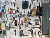 Wide view of pegboard with assorted hand tools and hardware items hung, including tape measures, pliers, clamps, scissors, and small hardware packs.