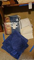 Photo of twin duvet cover, denim sheet set in original packaging, blue towels, and cream linens laid out on carpeted floor.