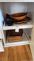 Wood bowls stacked with wooden salad utensils placed inside a large bowl, and wooden place mats below on shelving.