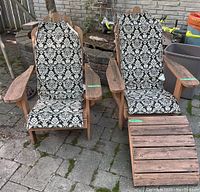 Photo showing two weathered wooden Adirondack chairs with black and white patterned cushions and one wooden ottoman on stone patio.