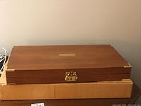 Wooden flatware case closed, resting on a brown cardboard box.
