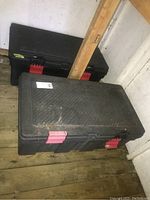 Photo of two large black plastic storage tubs with red locking latches, placed on wooden floor in a shed