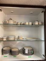 Full cabinet view showing shelves with organized dinnerware including teapot, cups, saucers, bowls, and stacks of plates