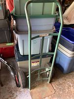 Front view of the metal frame hand truck dolly showing the full frame, handle, and base plate against storage bins in a garage.