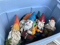 Blue plastic bin holding eight garden gnome figurines with varied colored hats and painted details.