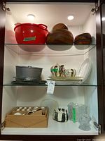 Wooden bowls, red serving bowl alongside metal bakeware and arrangement of plates and tea sets on glass shelves.