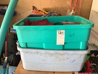 Two plastic totes stacked, a green one on top labeled 'Golf' and a gray one below with 'GME' written, likely containing golf accessories.