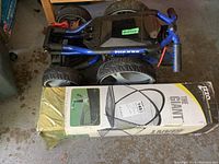 Folded blue Flip n' Go golf cart sitting on the ground with a large boxed golf practice net labeled 'The Giant' beneath it
