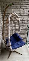 Front view of the wicker hanging hammock chair with blue cushion and rusted chain on metal stand.