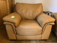 Front view of tan overstuffed leather armchair with wide armrests, smooth leather, and plush cushions.