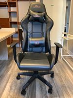 Front view of black ergonomic leather office chair with visible seat, backrest, and head/lumbar cushions embroidered with branding.