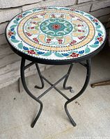 Full view of the round outdoor table with colorful decorative tile top and metal base.