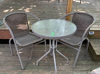 Two resin wicker chairs and one round table with glass top on wooden deck.