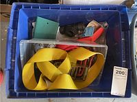 Top view of blue plastic bin containing yellow ratchet strap and assorted hardware including small PVC parts and metal components.
