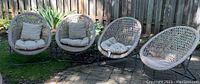Four weathered rattan scoop chairs outdoors, two with cushions and two without