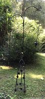 Full view of the two shepherd's hooks anchored in the ground alongside the wire plant stand outdoors in a yard with green shrubbery background.