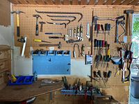 Wide view of pegboard with various hand tools including hammers, crowbars, axes, saws and other workshop implements hung and organized.