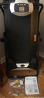 Full view of the Avari Fitness treadmill, folded upright showing the black running belt and control panel atop.