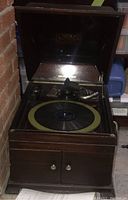 Front view of open Victrola showing the turntable with record, tonearm with horn speaker, and inside lid with branding.