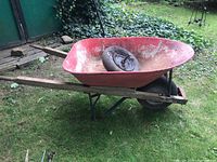 Red Erie wheelbarrow with wooden handles sitting on grass with a spare wheel inside the tub.