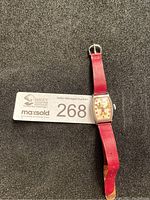 Full view of watch and red leather band next to auction tag