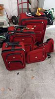 Photo showing all five pieces of the red luggage set arranged on floor, highlighting size differences and handles